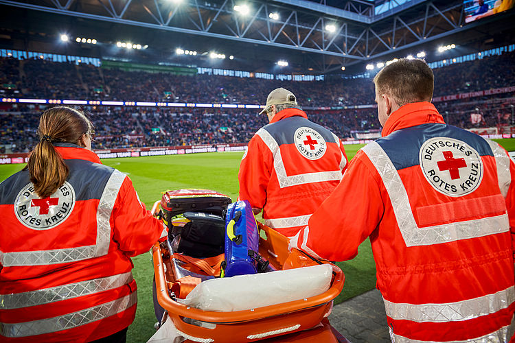 Einsatz des Sanitätsdienstes bei einem Fussballspiel Sanitäterin und Sanitäter im Stadion am Spielfeldrand mit einer fahrbaren Krankentrage.